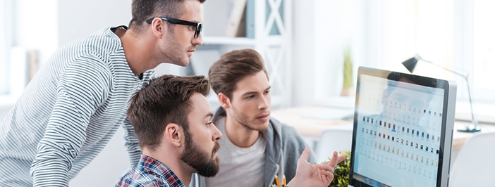 Tres hombres reunidos alrededor de la pantalla de una computadora, absortos en lo que ven.